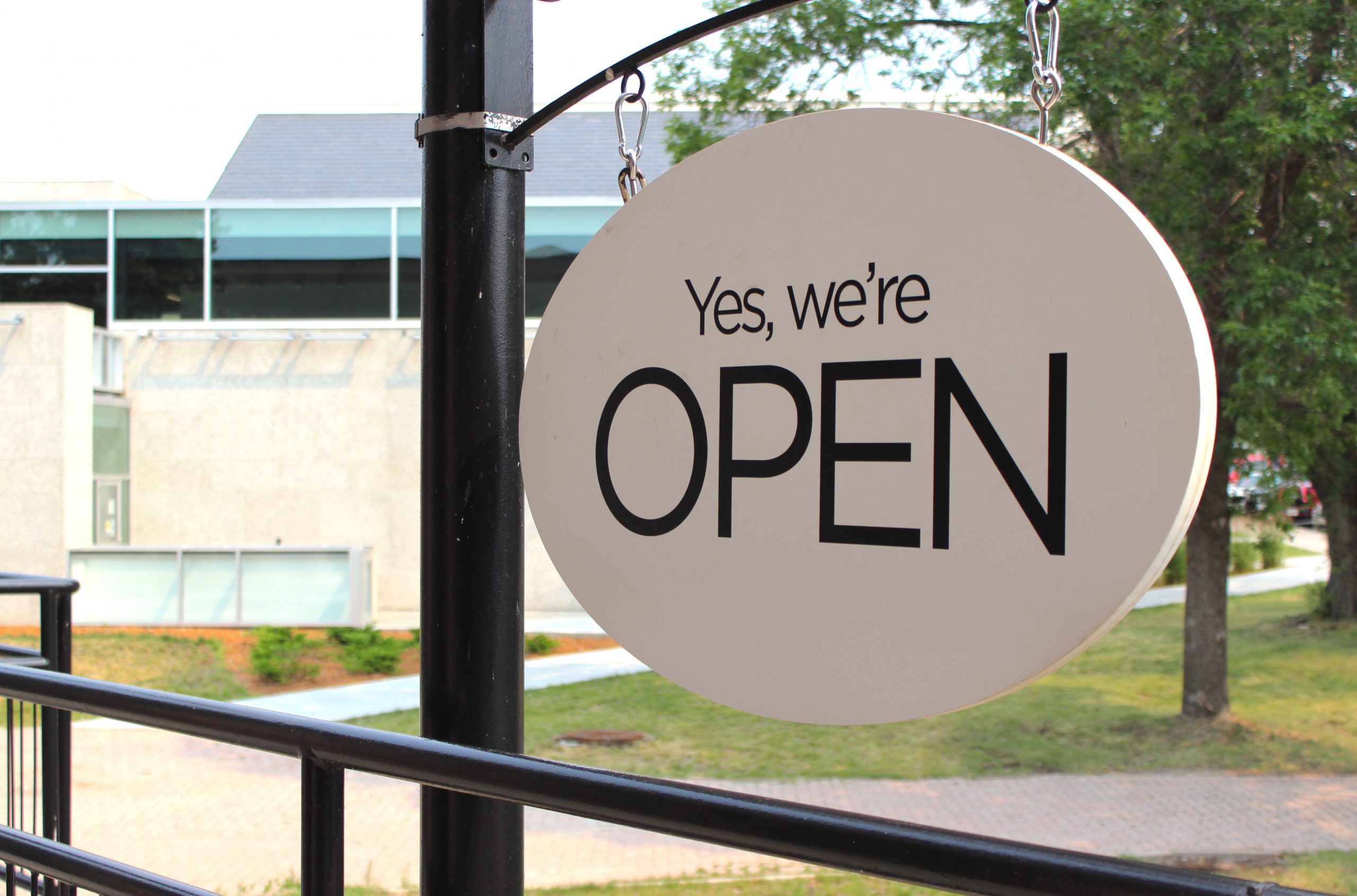 Photograph of a white sign reading "Yes, we're OPEN" in black text.