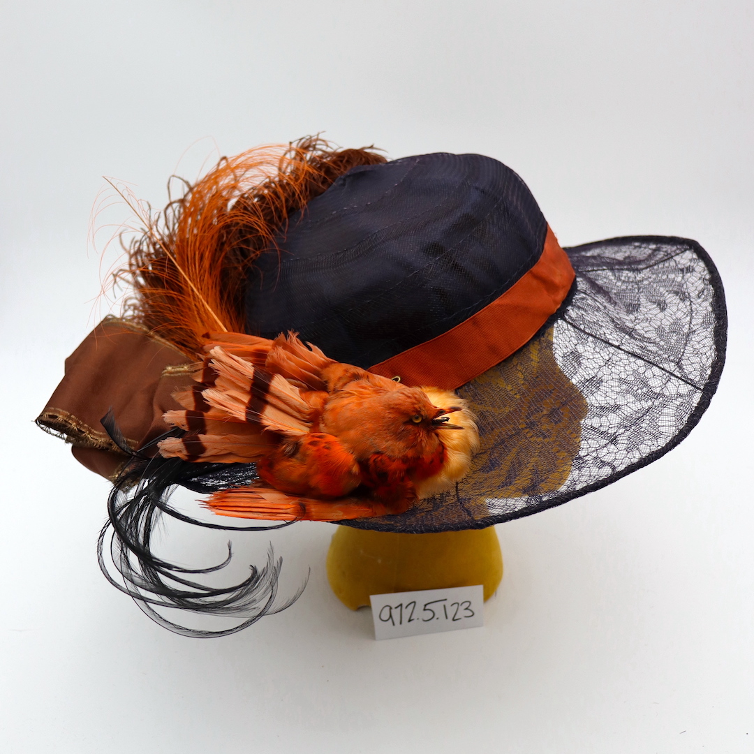An early 20th century hat featuring a stuffed orange bird.