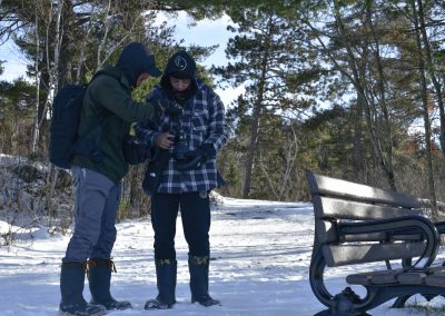Two students from Beaver Brae Secondary School ACE program holding and looking at cameras outside in the winter during their the Intro to Digital Photography class.