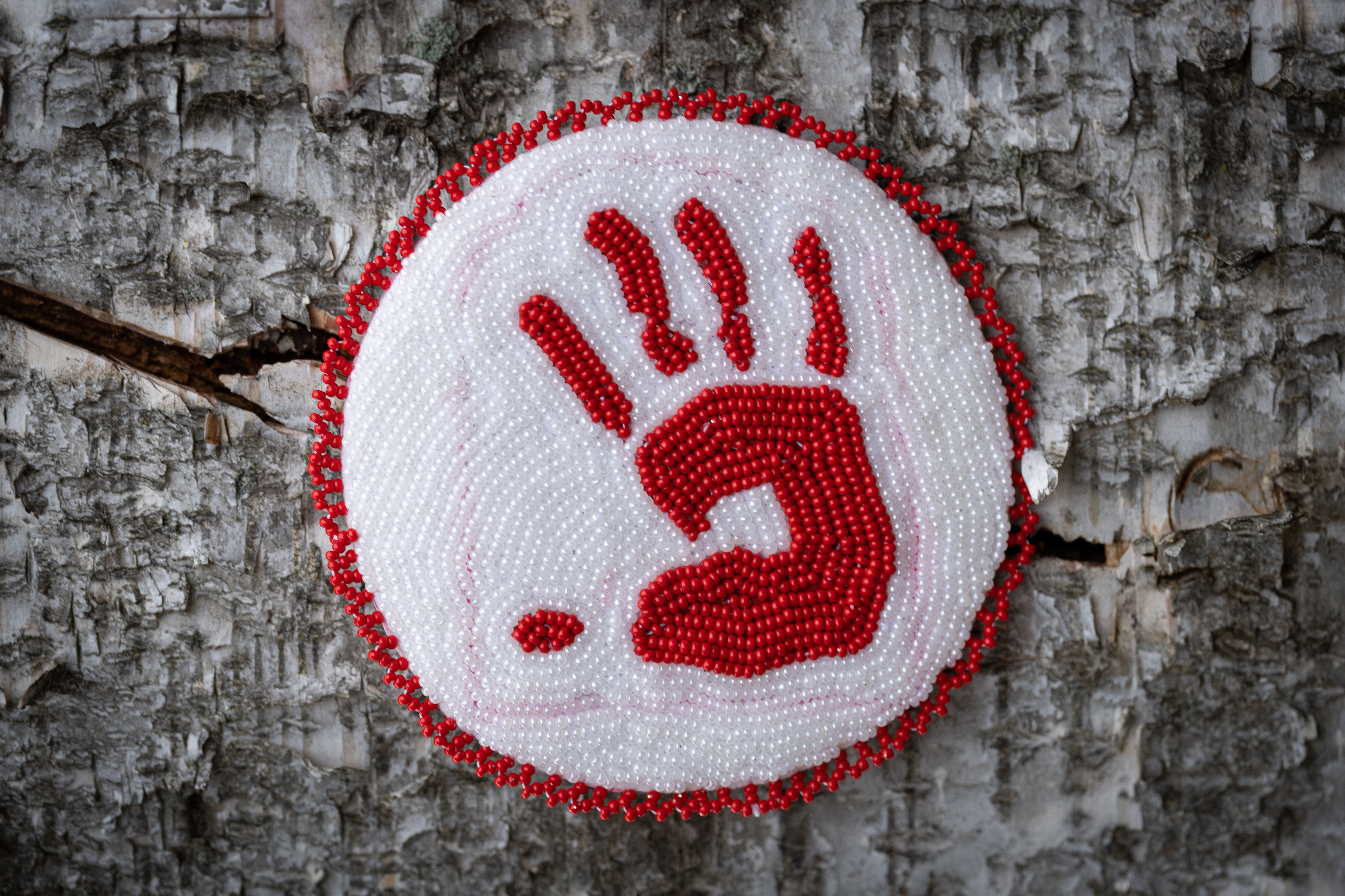 Round beaded amulet. Red beaded hand print in a white beaded surround.